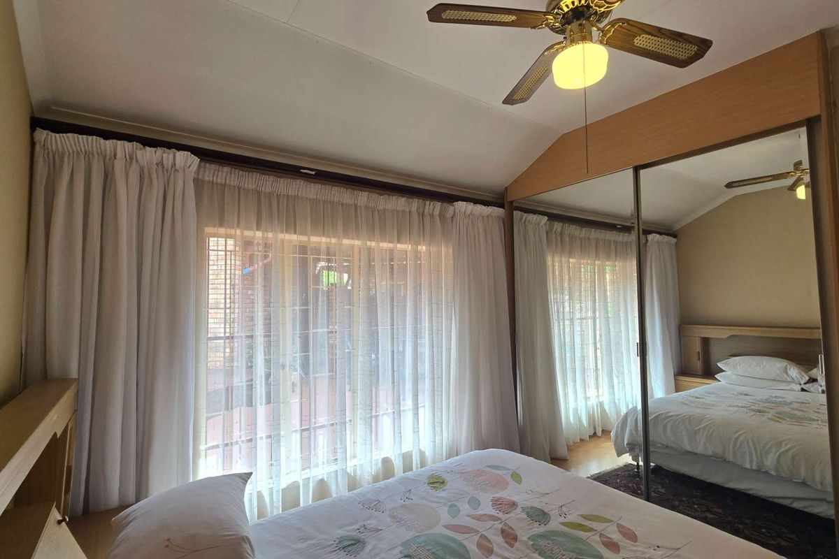 A bedroom featuring a ceiling fan and large built-in wardrobes with mirrored sliding doors, providing ample storage and natural light.