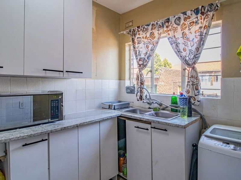 A functional kitchen featuring white built-in cabinetry, laminate countertops, a double stainless steel sink, and a tiled backsplash with natural light.