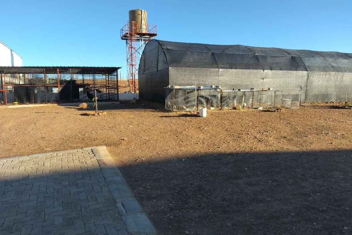 Outdoor area featuring a water tank, shade cloth tunnel structure, and fenced enclosures on a small holding property.