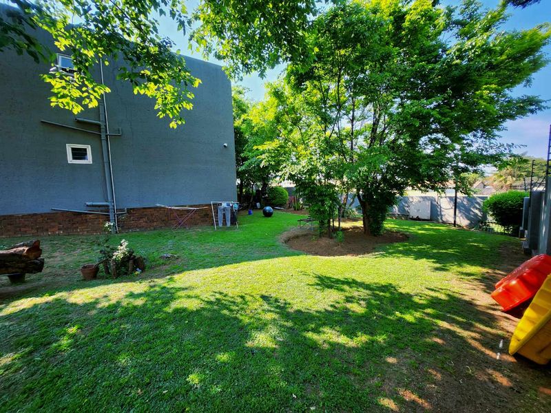 A spacious private garden area featuring a well-maintained lawn, mature trees, and perimeter walling, providing a peaceful outdoor space for the townhouse.