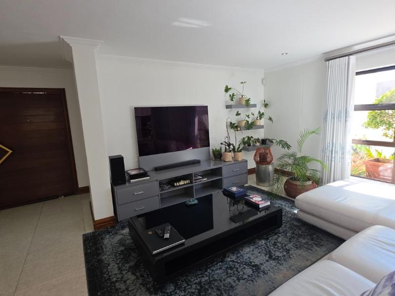 A bright and well-maintained living room featuring tiled flooring, modern cornicing, and large windows that provide ample natural light.