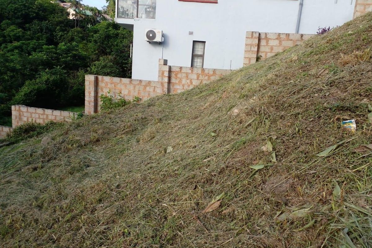A sloped residential plot featuring a tiered brick retaining wall and cleared vegetation, offering potential for terraced landscaping.