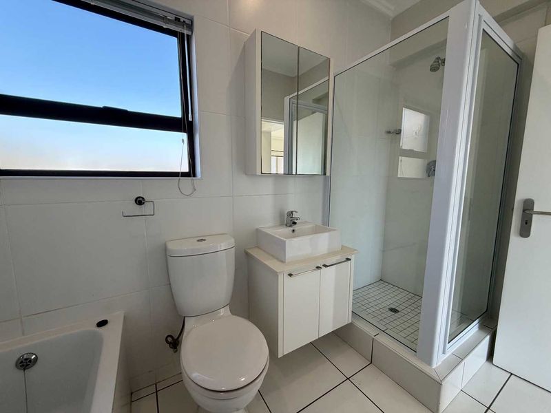 A clean, modern bathroom featuring a glass-enclosed shower, a separate bathtub, a wall-mounted vanity with a vessel sink, and a mirrored medicine cabinet.