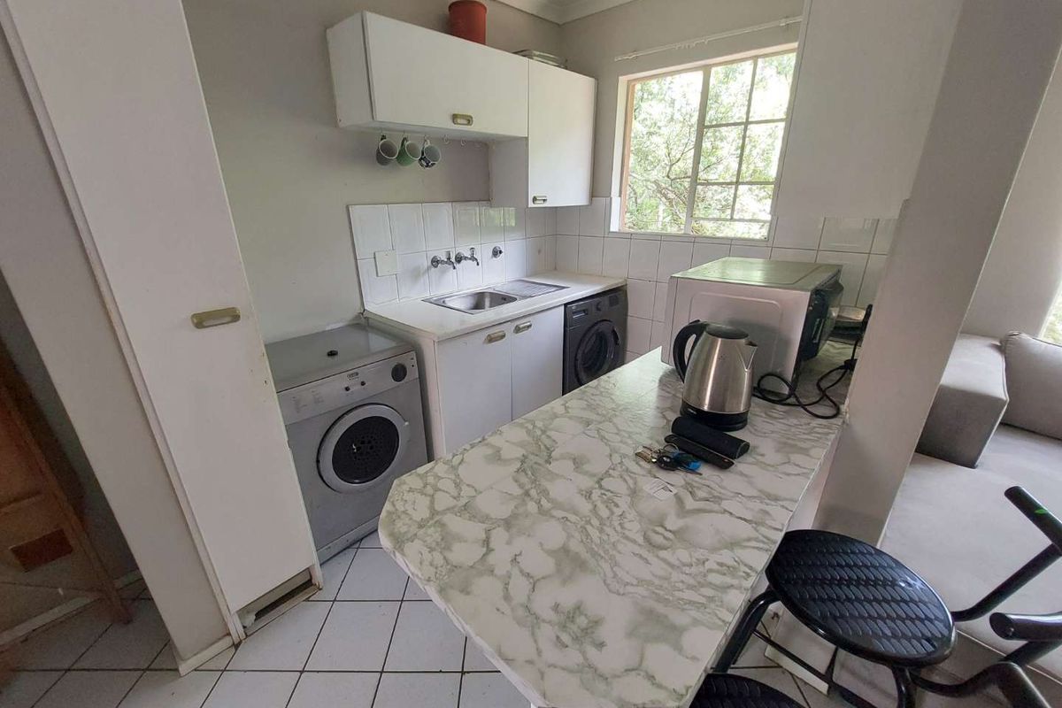 Compact kitchen area featuring white cabinetry, a stainless steel sink, tiled backsplash, and a marble-effect breakfast bar counter.