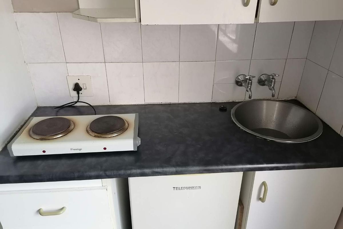 A compact kitchen area featuring a laminate countertop, stainless steel sink, tiled splashback, and built-in cabinetry.