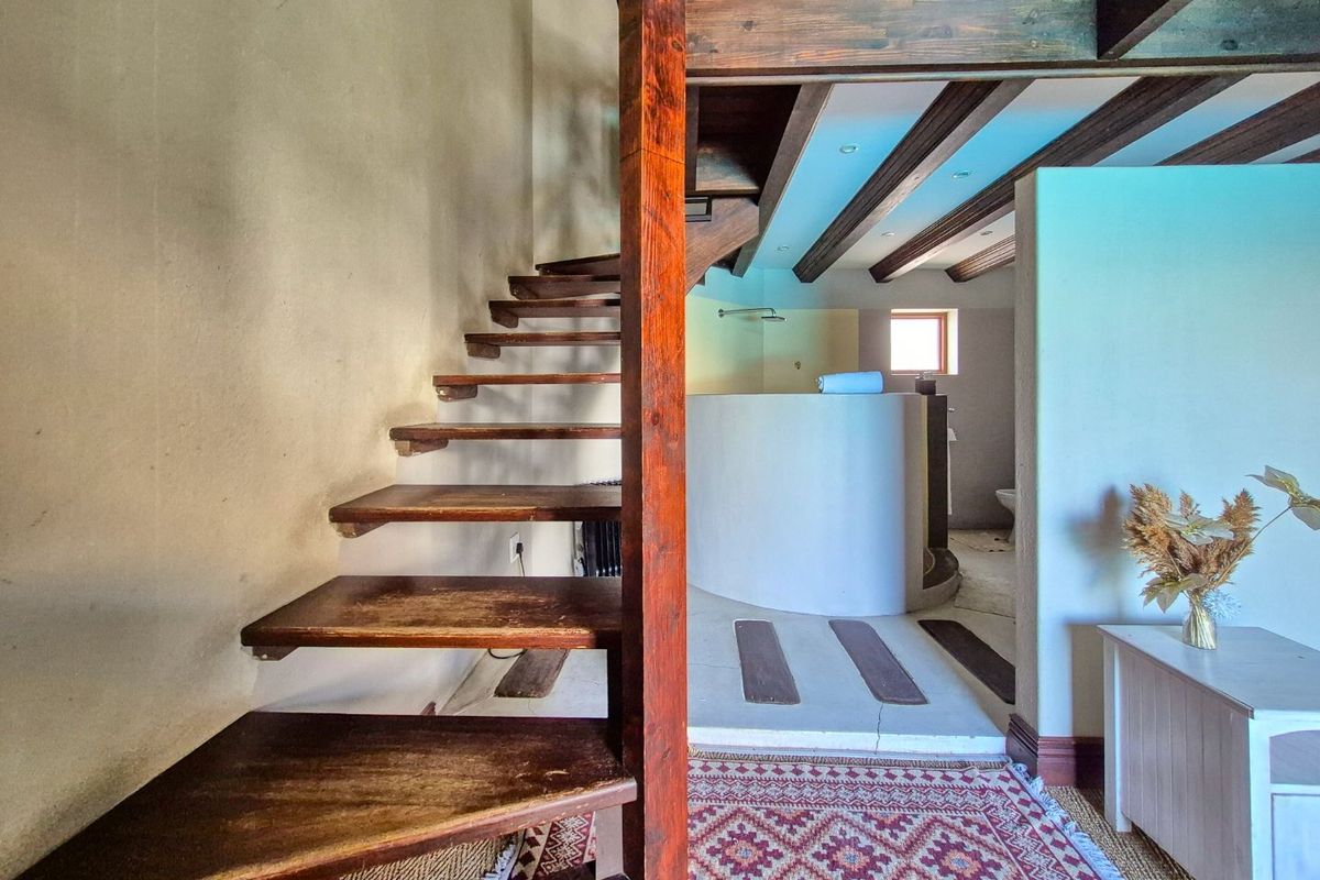 A unique bedroom featuring a wooden staircase leading to a loft, exposed ceiling beams, and an open-plan en-suite bathroom with a curved shower partition.