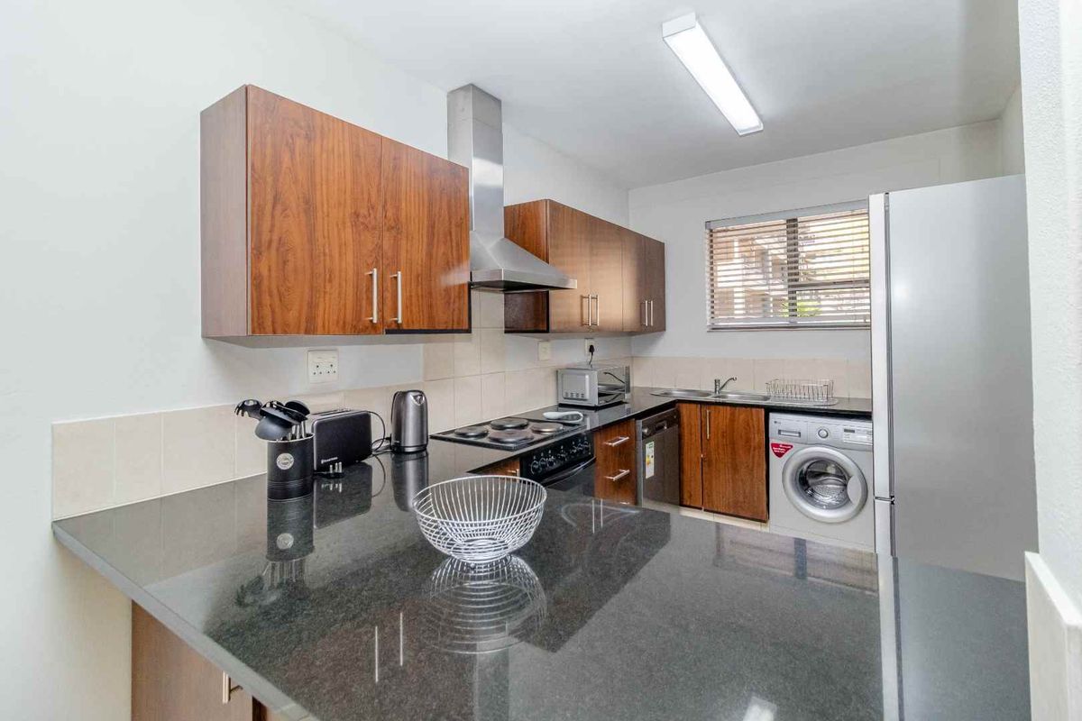 A functional kitchen featuring wood veneer cabinetry, granite countertops, a stainless steel extractor fan, and integrated space for laundry appliances.