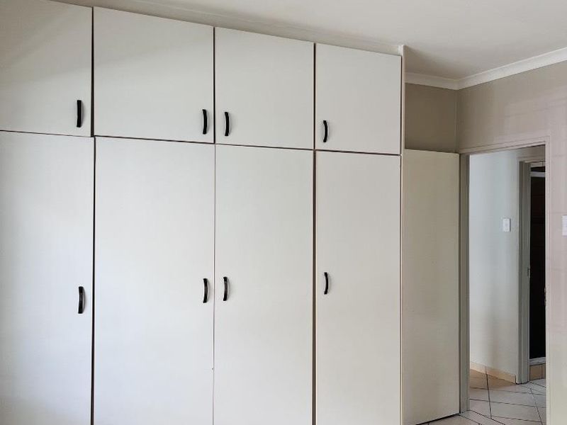 A clean, empty bedroom featuring floor-to-ceiling built-in cupboards and neutral tiled flooring, offering a versatile space ready for personalization.