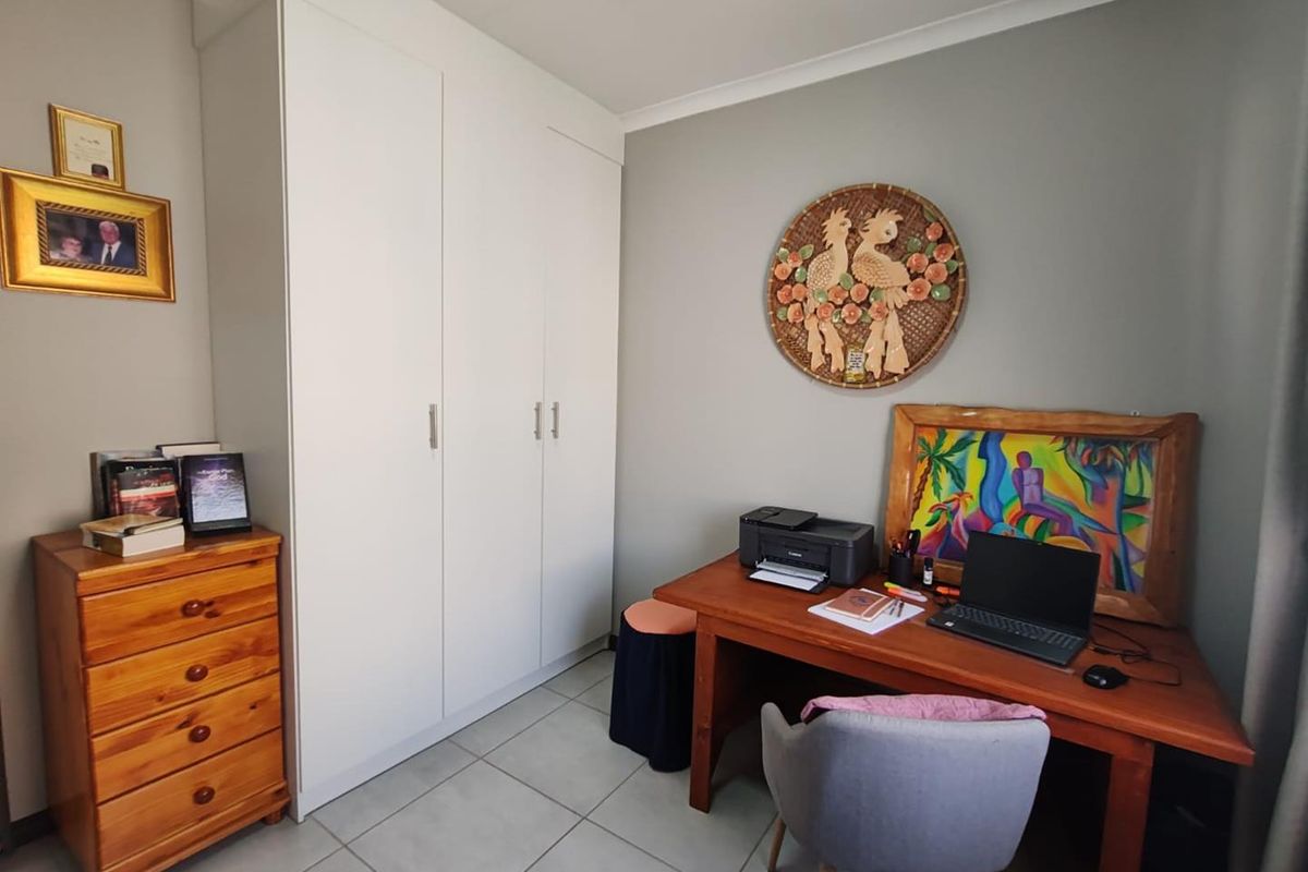 A functional bedroom featuring built-in cupboards and tiled flooring, currently utilized as a home office space.