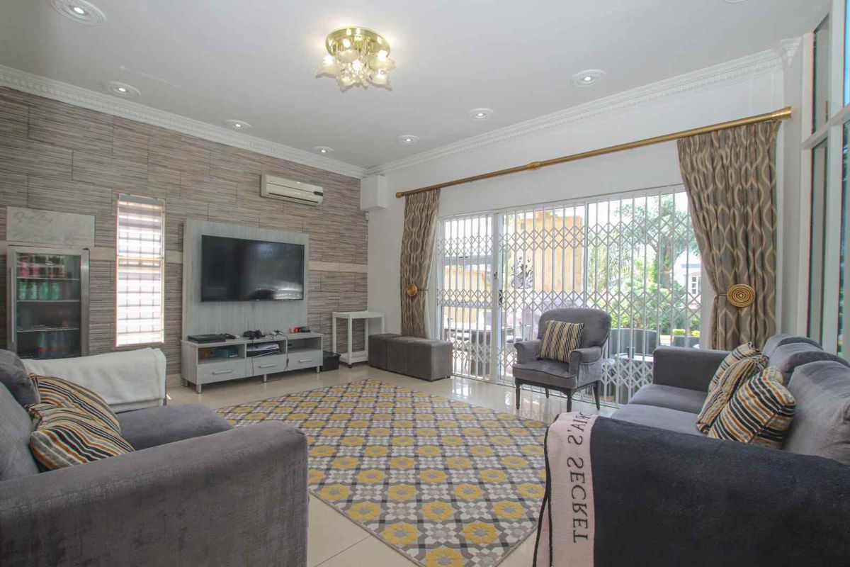 Spacious living room featuring tiled flooring, recessed ceiling lighting, a textured feature wall, and sliding glass doors leading to an outdoor patio area.