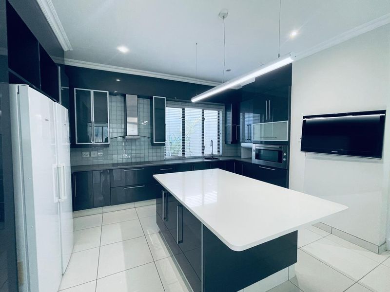 Modern kitchen featuring high-gloss cabinetry, a central island with quartz countertops, built-in appliances, and sleek tiled finishes in a bright, contemporary space.
