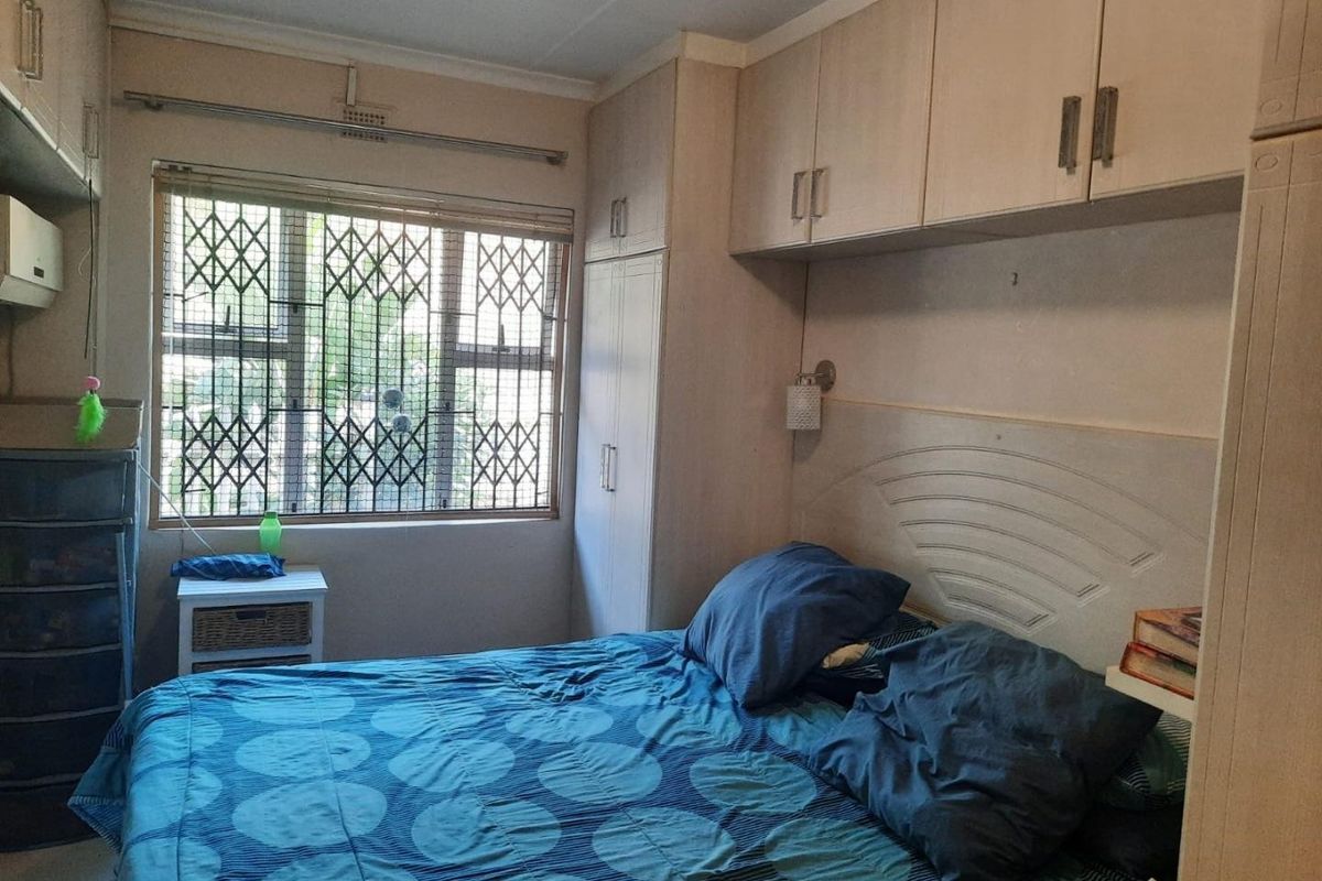A bedroom featuring built-in cupboards and a window fitted with a security gate, providing functional storage and natural light.