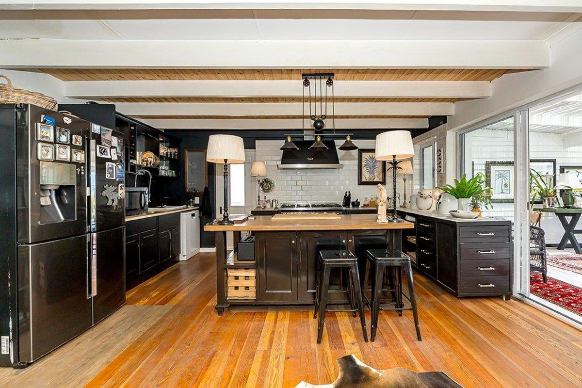 A spacious kitchen featuring dark cabinetry, a central island with a wooden countertop, subway tile backsplash, and exposed wooden ceiling beams.