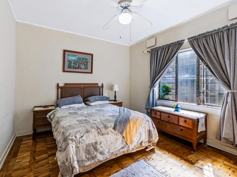 A bedroom featuring parquet flooring, a ceiling fan, and a window fitted with security bars.