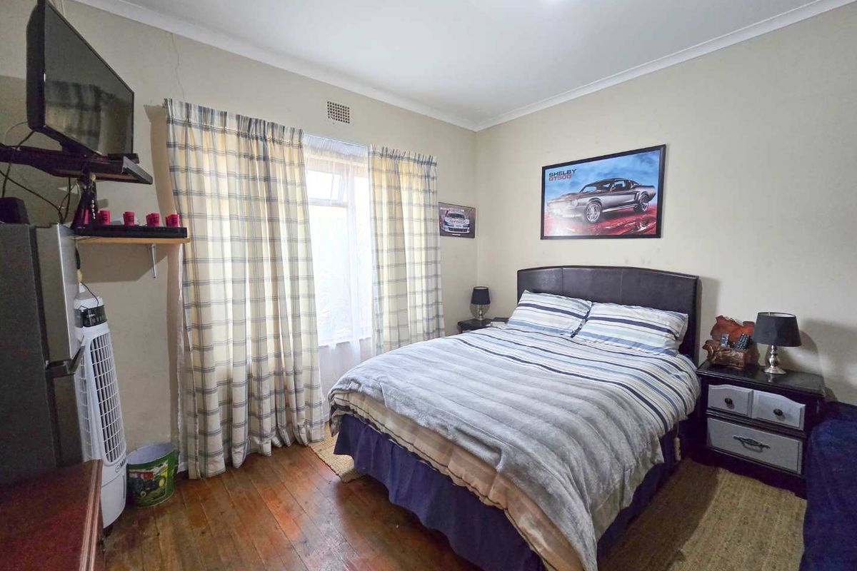 A functional bedroom featuring timber flooring, a central window with curtains, and standard ceiling lighting.
