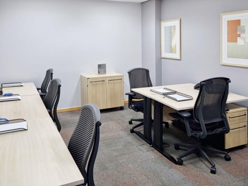 A functional office space featuring neutral wall tones, carpeted flooring, and integrated desk configurations suitable for a professional work environment.