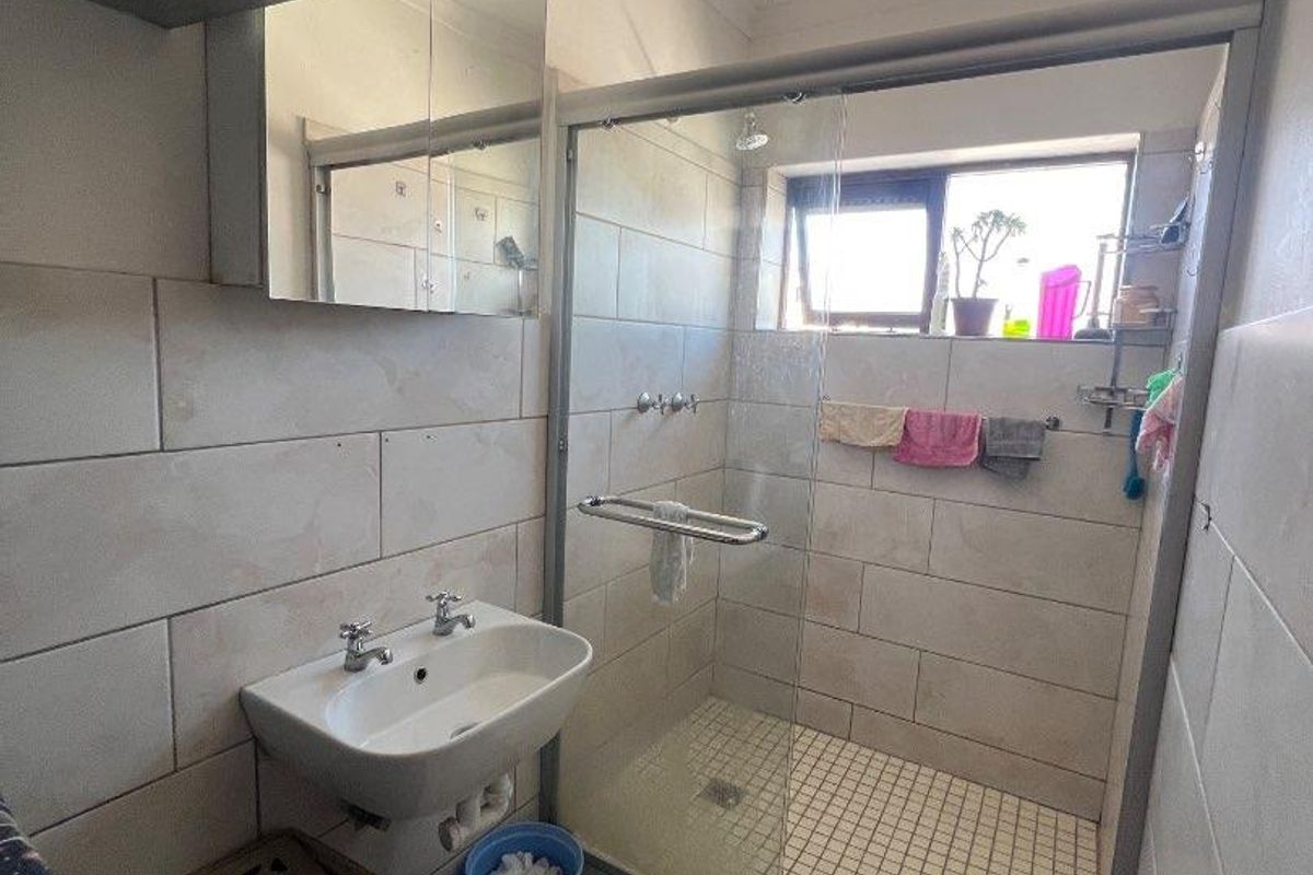 A functional bathroom featuring a glass-enclosed shower, wall-mounted basin, and tiled finishes throughout.