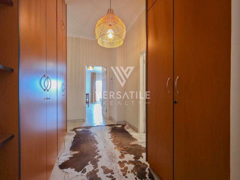 A well-lit hallway featuring extensive built-in wooden cabinetry for storage and neutral tiled flooring.