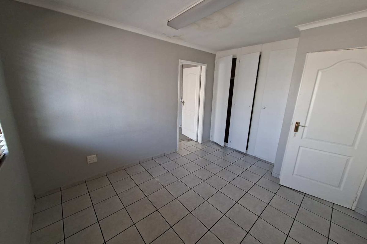 An empty bedroom featuring tiled flooring, built-in cupboards, and a neutral grey wall finish, requiring minor ceiling repairs.