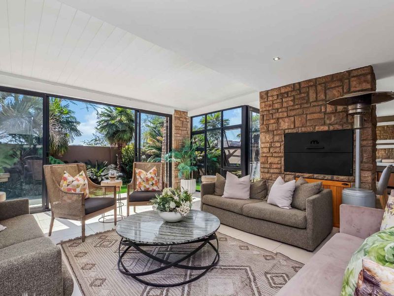Spacious living area featuring a prominent stone fireplace, built-in braai, and large sliding glass doors that provide seamless access to the garden.