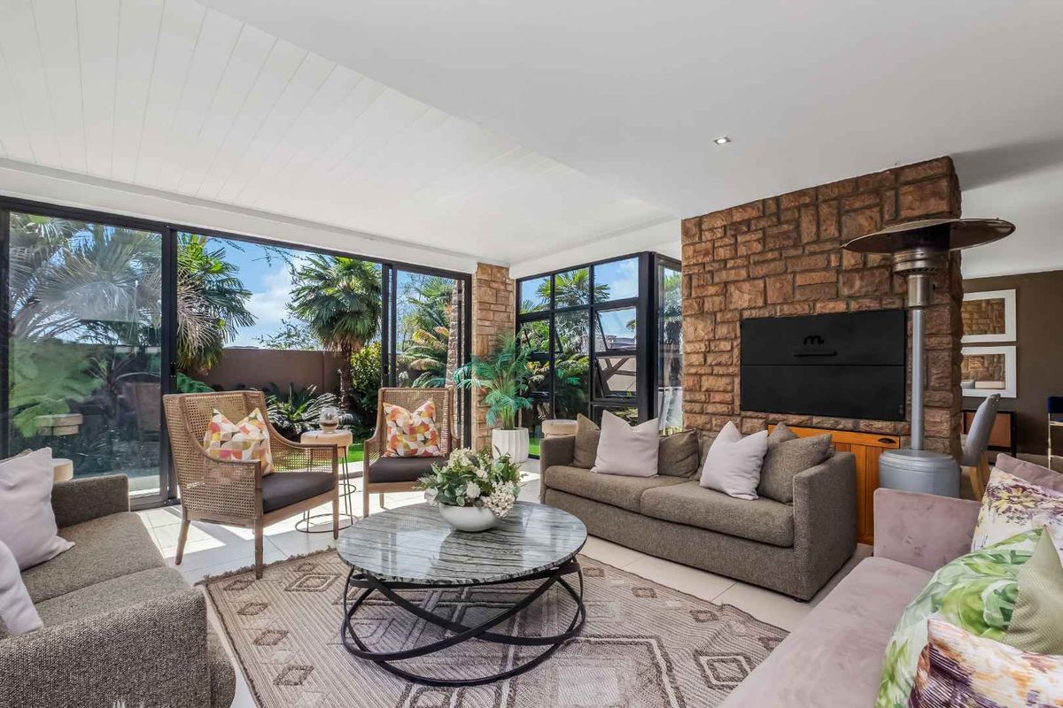 Spacious living area featuring a prominent stone fireplace, built-in braai, and large sliding glass doors that provide seamless access to the garden.