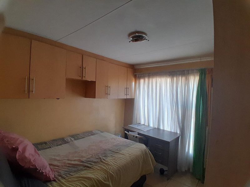 A bedroom featuring built-in wooden cupboards and a window with curtains, requiring minor repairs to the ceiling light fixture.