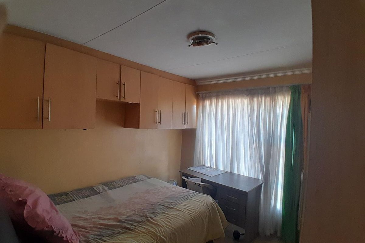 A bedroom featuring built-in wooden cupboards and a window with curtains, requiring minor repairs to the ceiling light fixture.