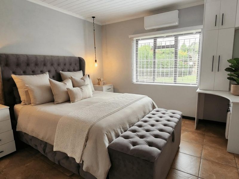 A well-maintained bedroom featuring built-in cabinetry, tiled flooring, a split-system air conditioner, and a window with security bars.