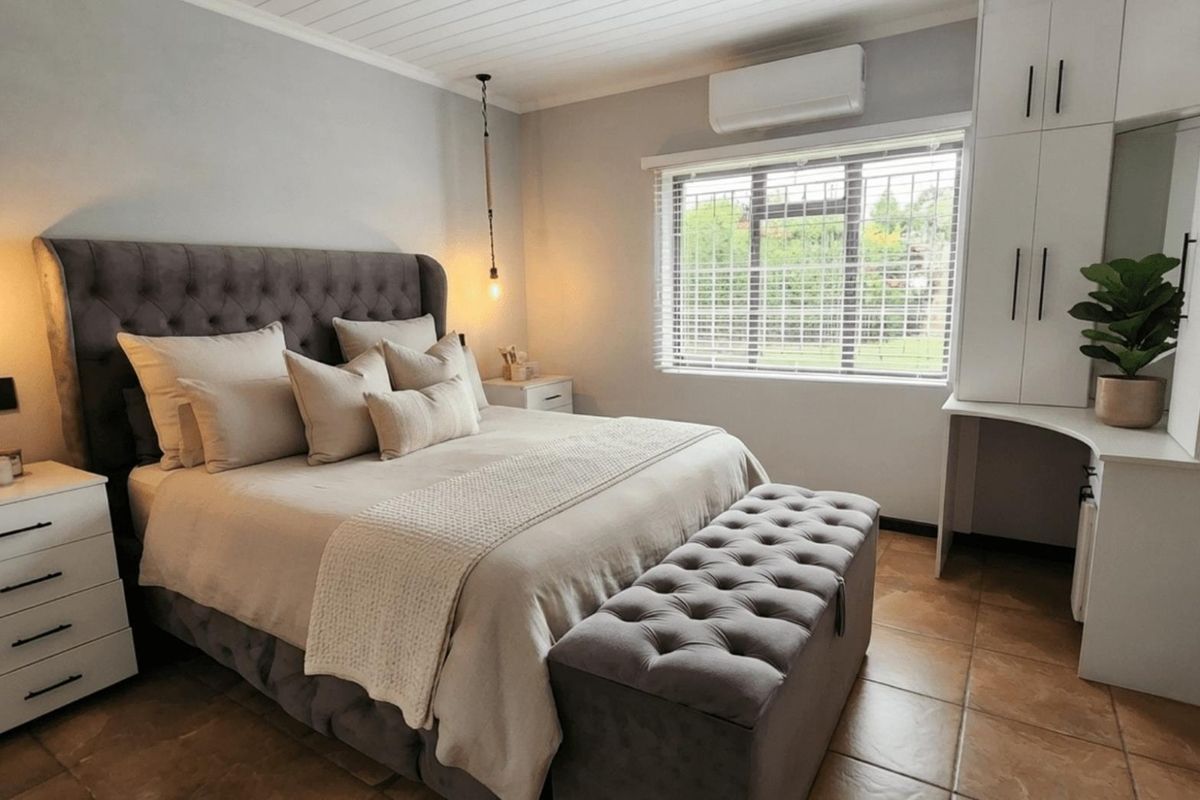 A well-maintained bedroom featuring built-in cabinetry, tiled flooring, a split-system air conditioner, and a window with security bars.