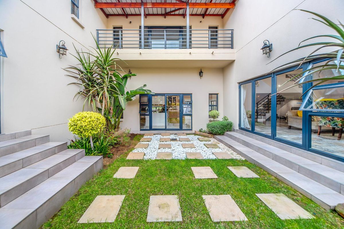 A well-maintained rear courtyard featuring a landscaped garden with paver pathways, tiled stairs, and a balcony overlooking the outdoor space.
