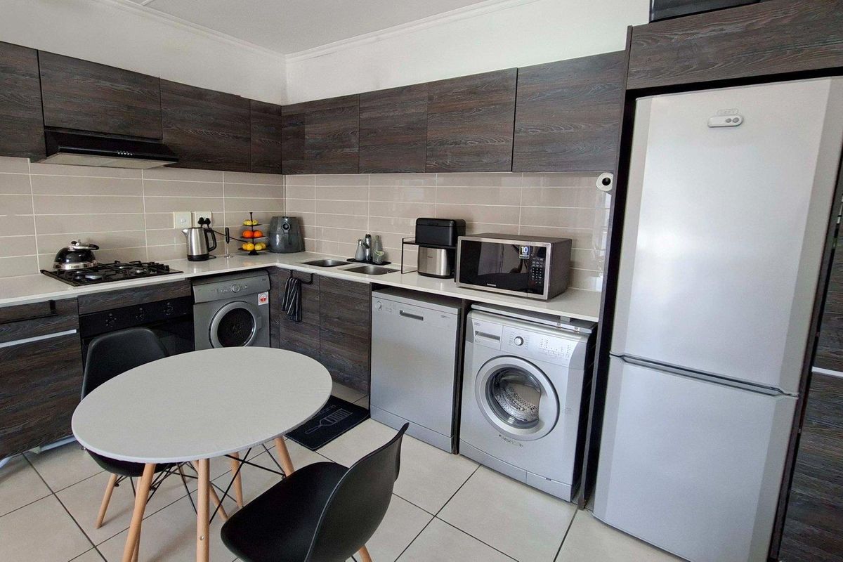 Modern kitchen featuring dark wood-grain cabinetry, light stone-look countertops, tiled backsplash, and integrated space for laundry appliances.