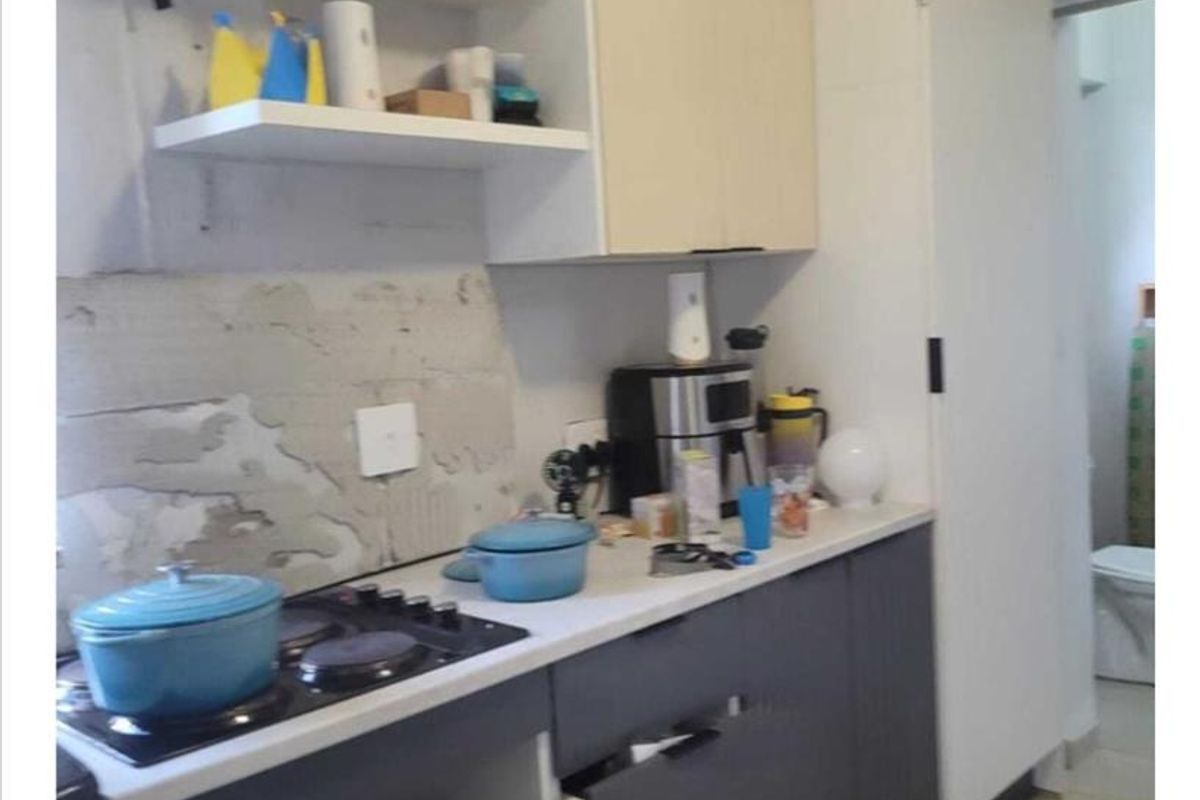 Compact kitchen featuring built-in cabinetry, a hob, and microwave space, currently requiring wall finishing and minor repairs to cabinetry.