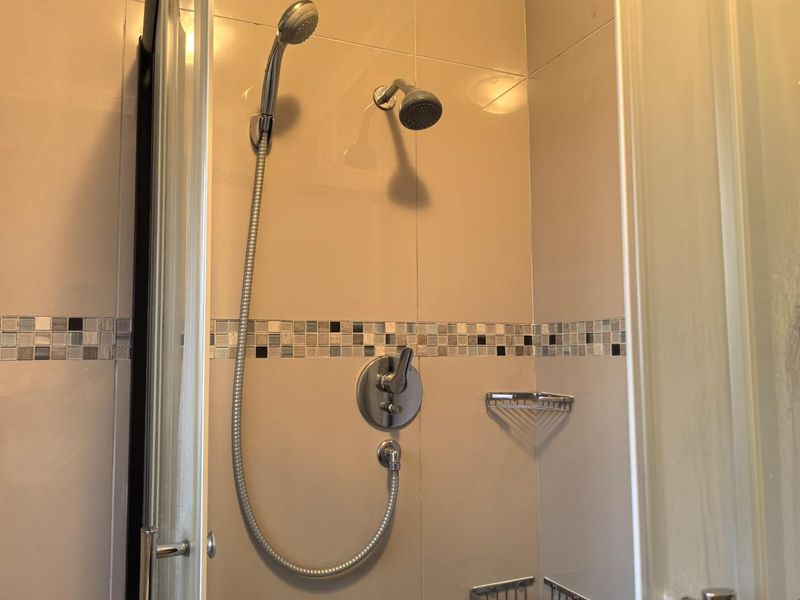 A functional shower enclosure featuring a dual shower head system, chrome mixer tap, and decorative mosaic tile accents on the wall.
