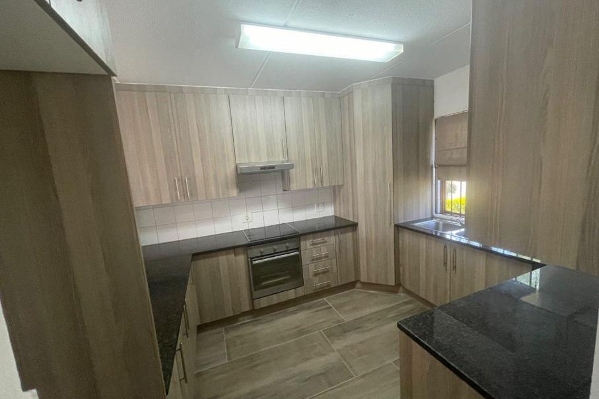 A functional kitchen featuring wood-look laminate cabinetry, dark granite countertops, built-in oven, electric hob, and tiled flooring.