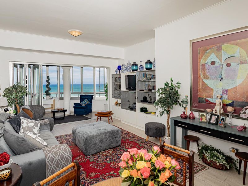 Spacious living room featuring built-in shelving, light-toned laminate flooring, and large sliding glass doors that open to a balcony with ocean views.