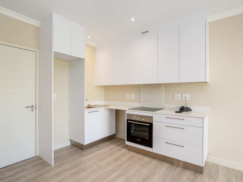 Modern kitchen featuring white cabinetry, integrated electric hob and oven, stainless steel sink, and light wood-look laminate flooring.