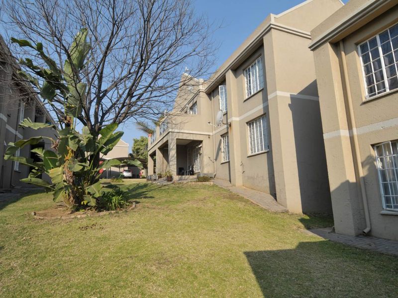Rear view of the apartment complex featuring a shared garden area, paved walkways, and exterior building facade with security window bars.