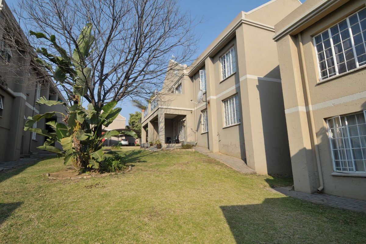 Rear view of the apartment complex featuring a shared garden area, paved walkways, and exterior building facade with security window bars.