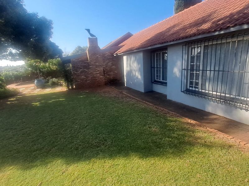 Rear view of the house featuring a brick chimney, tiled roof, and security bars on windows, overlooking a well-maintained lawn.