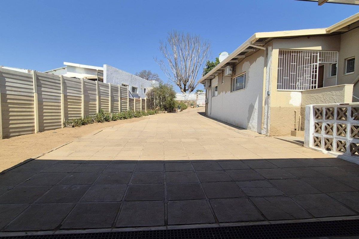 A paved side driveway and rear exterior area featuring a precast boundary wall and security bars on the windows.