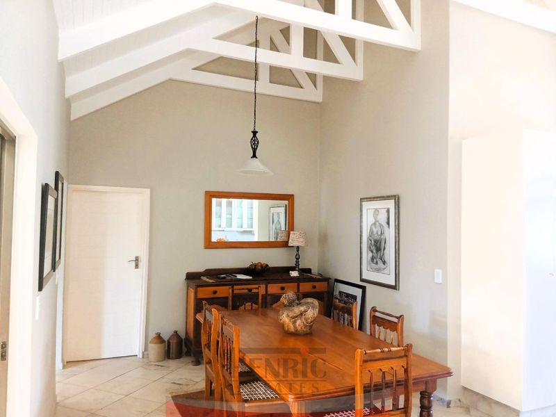 Spacious dining room featuring a high vaulted ceiling with exposed white timber trusses, tiled flooring, and elegant pendant lighting.