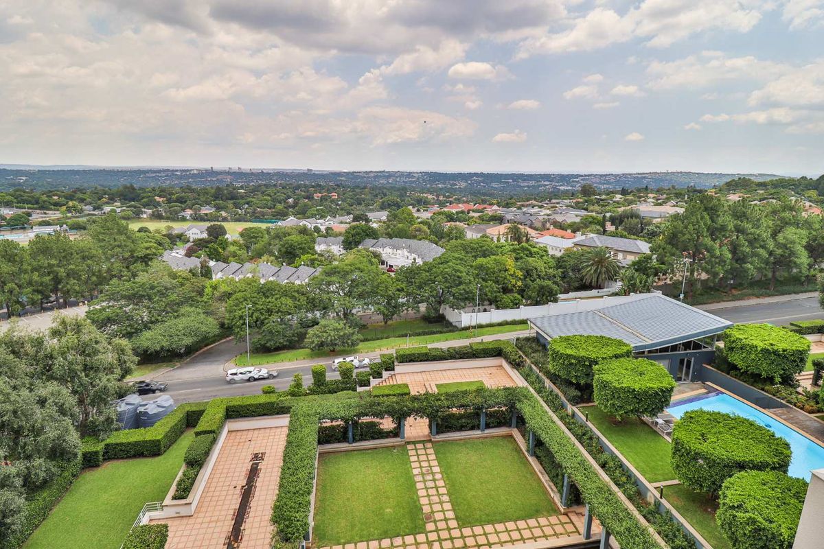 Aerial view of the apartment complex grounds featuring a swimming pool, manicured gardens, paved terrace areas, and established landscaping.