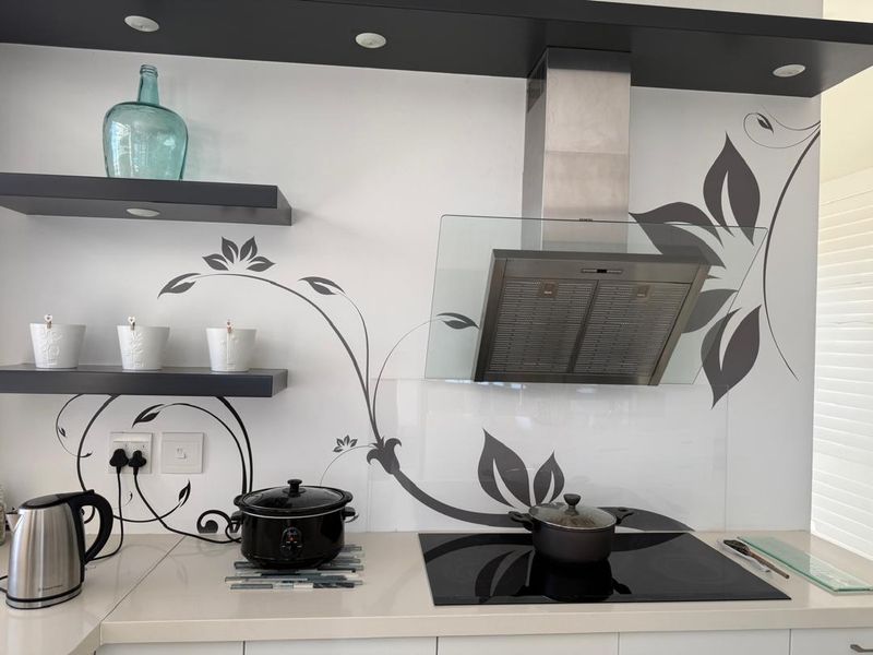 Modern kitchen area featuring a sleek induction cooktop, stainless steel extractor fan, glass splashback with floral detailing, and floating shelving.