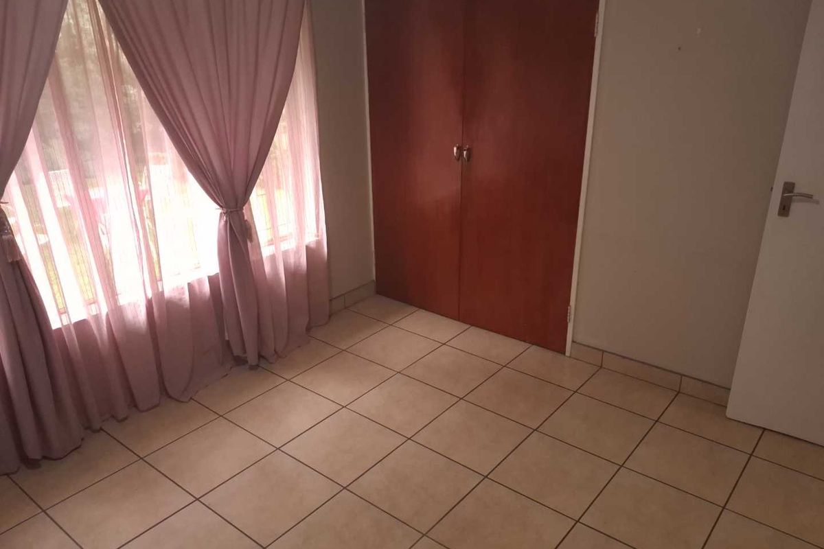 A bedroom featuring tiled flooring and built-in wooden cupboards, offering a functional space with natural light.