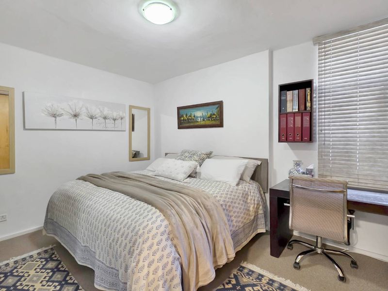 A well-maintained bedroom featuring neutral walls, carpeted flooring, built-in shelving, and venetian blinds for natural light control.