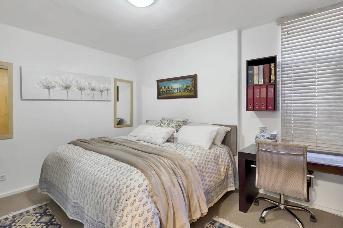 A well-maintained bedroom featuring neutral walls, carpeted flooring, built-in shelving, and venetian blinds for natural light control.