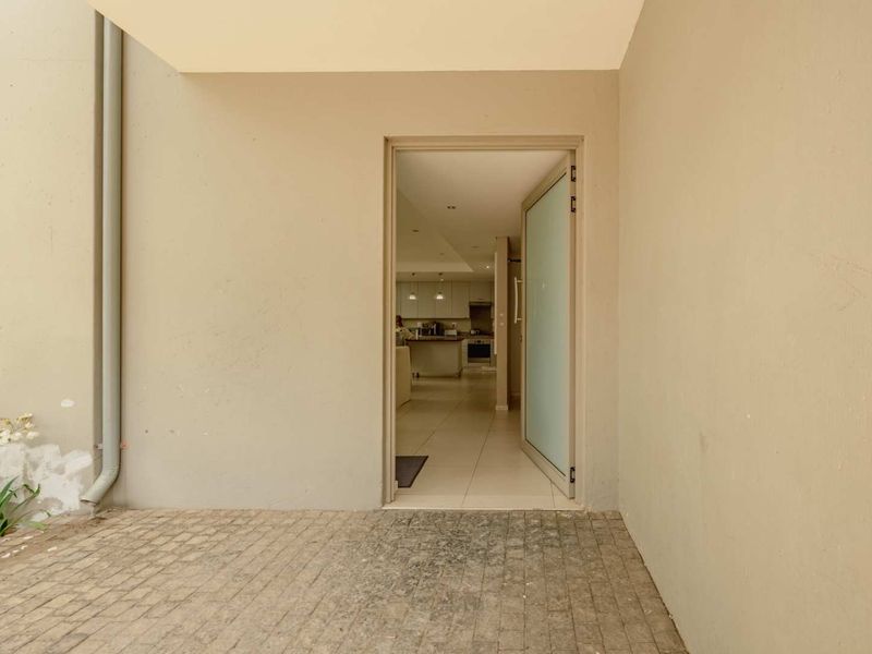 A covered patio area featuring paved flooring and a frosted glass entrance door leading into the main living space.