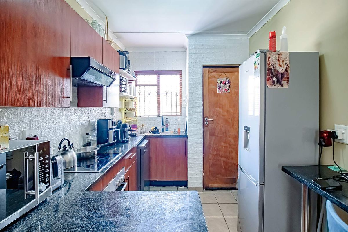 A functional kitchen featuring dark granite countertops, wood-finish cabinetry, a built-in hob, and an extractor fan, with tiled flooring throughout.