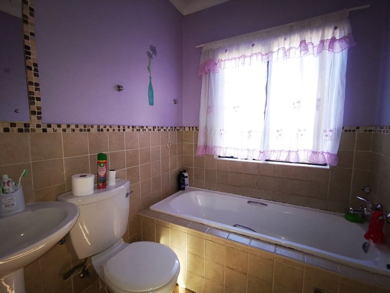 A functional bathroom featuring a built-in bathtub, pedestal basin, and toilet, finished with neutral wall tiles and a decorative mosaic border.