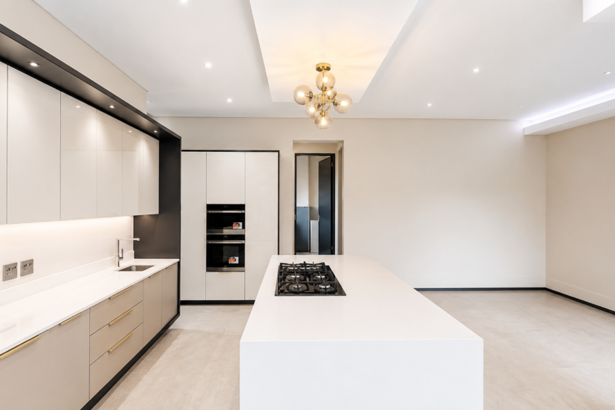 Modern, high-end kitchen featuring a large central island with a gas cooktop, sleek cabinetry, built-in double ovens, and premium stone countertops.